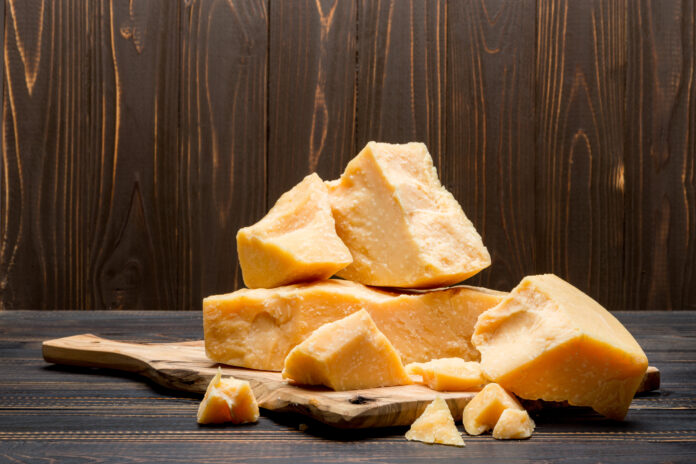 Pedaços de Parmigiano-Reggiano autêntico sobre uma tábua de madeira, com fundo rústico.