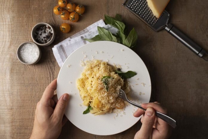 Prato de arroz italiano cremoso com queijo ralado e folhas de manjericão em uma mesa de madeira rústica.