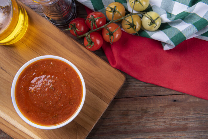 Molho de tomate caseiro em tigela branca com tomates frescos ao lado