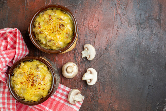 Prato de polenta cremosa servida em cumbucas individuais, acompanhada por cogumelos frescos decorativos e um guardanapo xadrez vermelho.