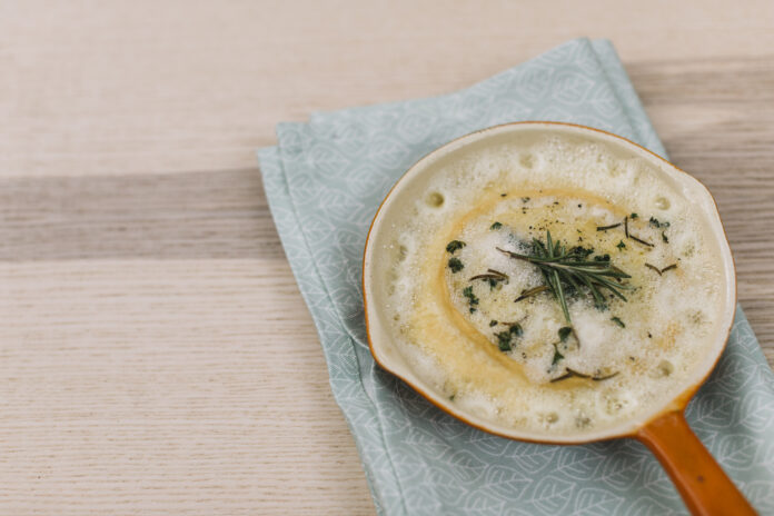 Prato de Zuppa Toscana servido em um bowl com acabamento cremoso e decorado com ervas frescas sobre um guardanapo verde.