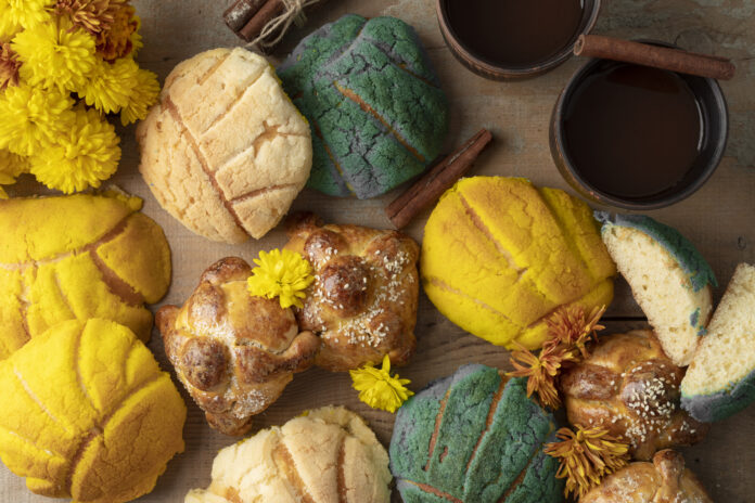 Pães artesanais variados com flores e canela ao lado de xícaras de café.