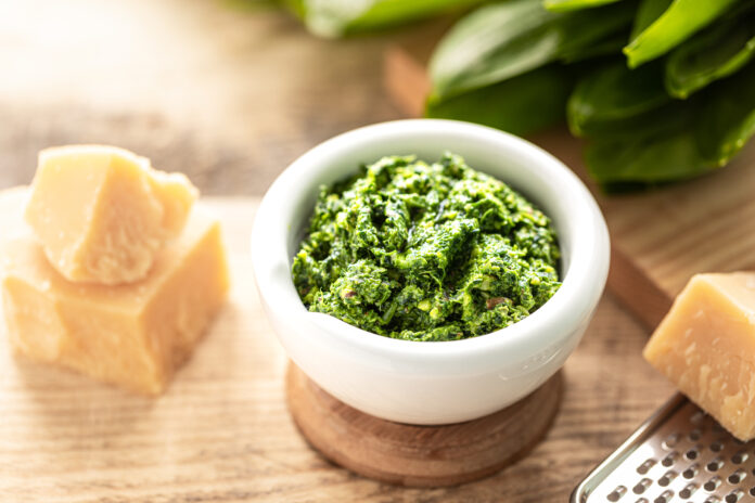 Pesto genovese autêntico em um pilão de cerâmica branca com pedaços de parmesão ao lado.