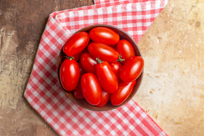 Tomates San Marzano frescos em uma tigela de madeira sobre uma toalha xadrez vermelha.