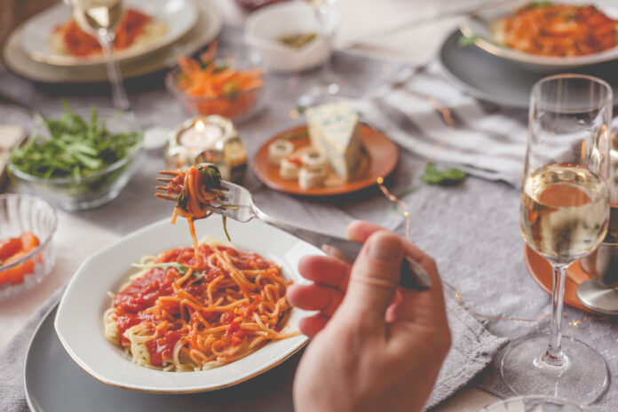 Prato de espaguete ao molho de tomate servido em uma mesa decorada para um jantar italiano com vinho e acompanhamentos.