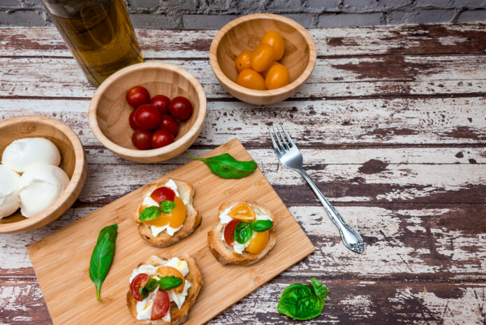 Aperitivos italianos com bruschettas de tomate, manjericão e mozzarella fresca sobre uma tábua de madeira.