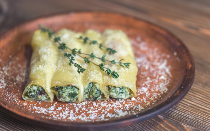 Cannelloni recheado com espinafre e ricota servido em prato rústico com ramos de tomilho fresco e parmesão ralado.