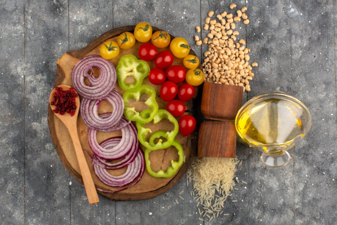 Ingredientes frescos para uma dieta mediterrânea com toque italiano, incluindo cebola roxa, pimentão verde, tomates cereja, arroz, feijão-fradinho e azeite.