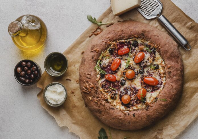 Pizza integral com massa saudável, coberta com tomates-cereja, azeitonas pretas, rúcula e queijo parmesão.