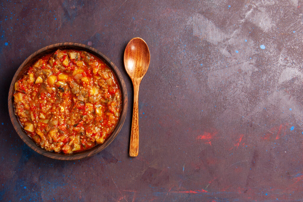 Tigela de ragù italiano servido em um prato rústico, acompanhado de uma colher de madeira sobre uma mesa texturizada.