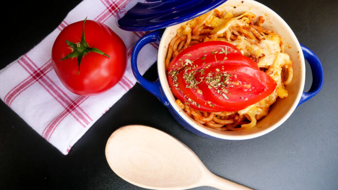 Prato de massa ao molho de tomate com fatias frescas de tomate, servido em uma tigela azul.