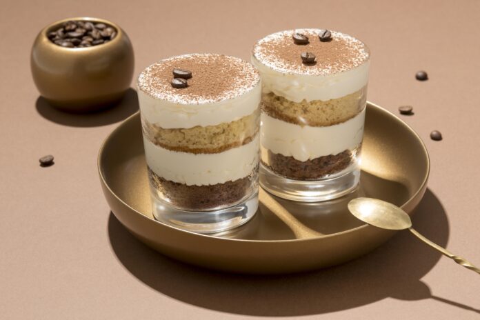 Taças de tiramisù low carb decoradas com grãos de café e cacau, servidas em um prato dourado, acompanhadas por uma colher.