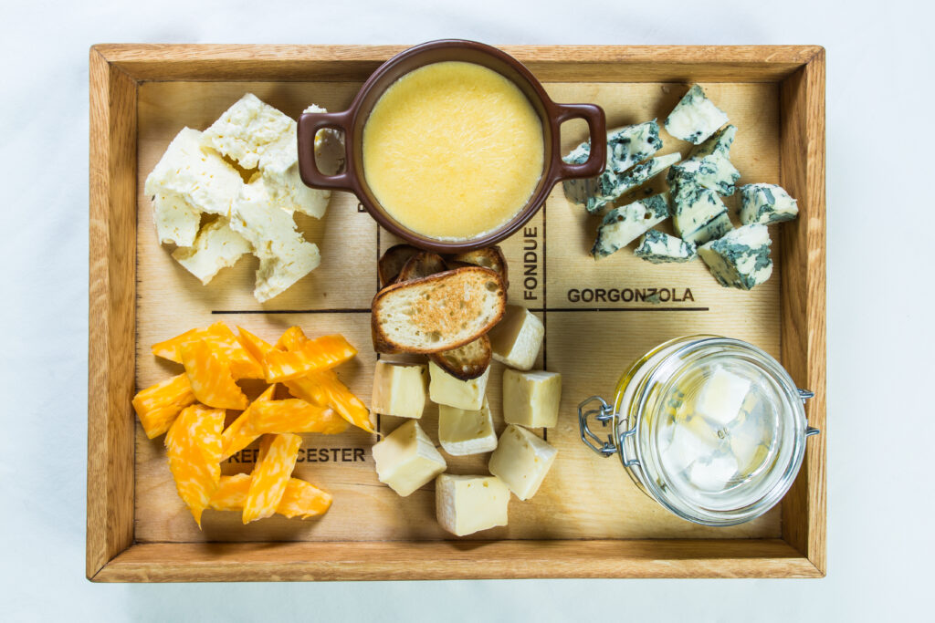 Tábua com variedades de queijos e fondue, representando os sabores alpinos da culinária italiana.