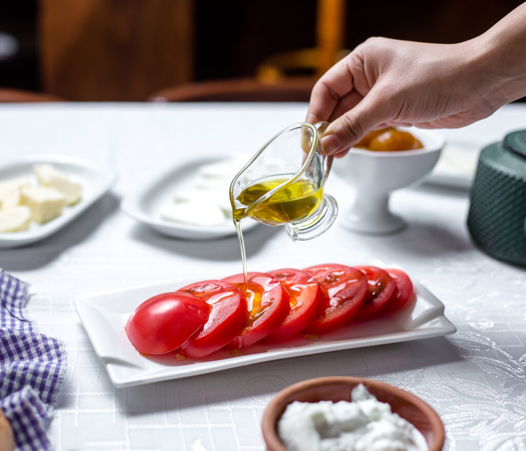 Mão derramando vinagre balsâmico sobre tomates fatiados em um prato branco.